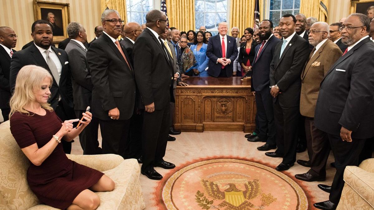 Kellyanne Conway, de rodillas sobre el sofá, consulta su móvil mientras Trump y sus invitados posan para la foto oficial.