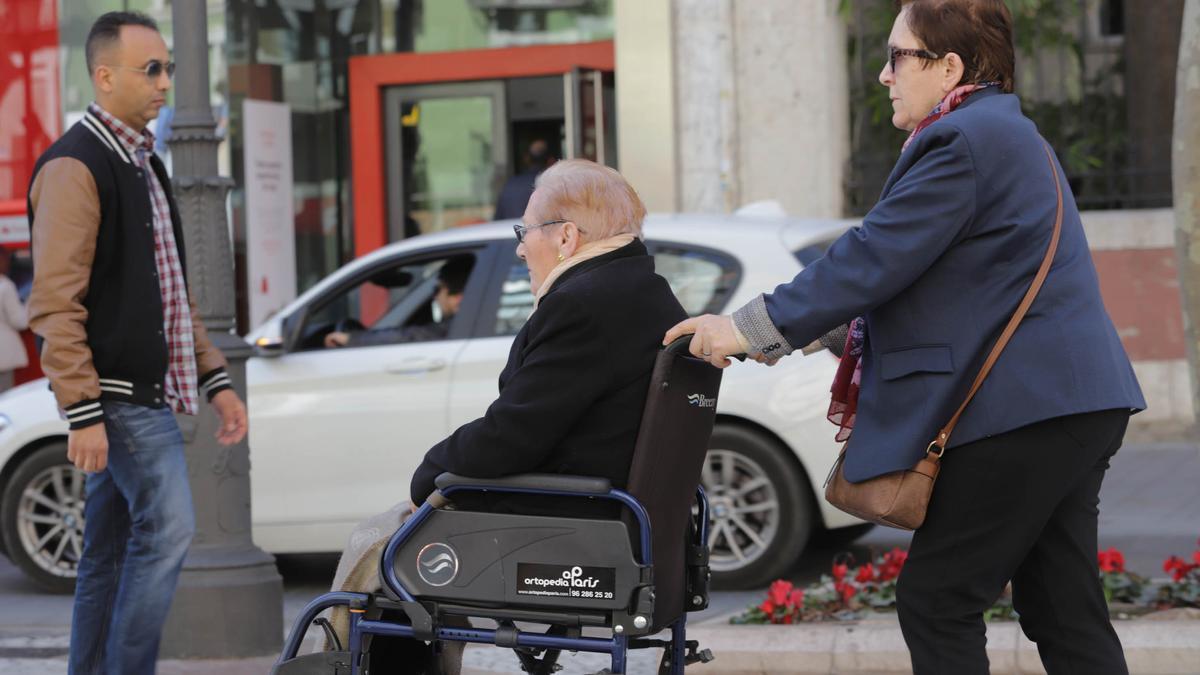 Una mujer en silla de ruedas es empujada por otra en València.