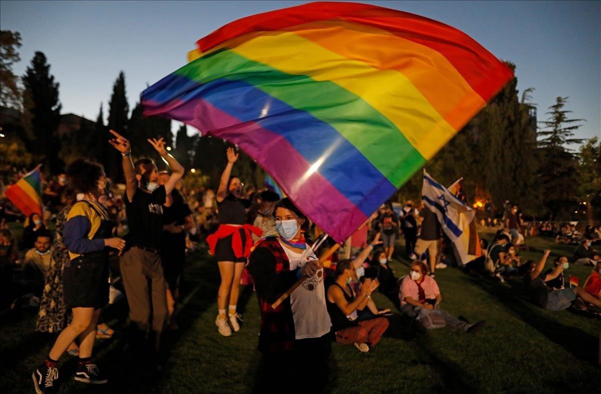 Un participante vestido con una máscara ondea la bandera del arco iris, mientras otros celebran el desfile anual del Orgullo de Jerusalén en medio de la pandemia COVID-19.