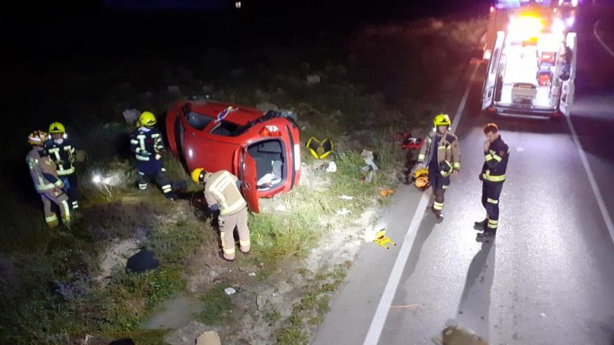 Los bomberos tratan de rescatar al matrimonio del interior del vehículo volcado tras el accidente.