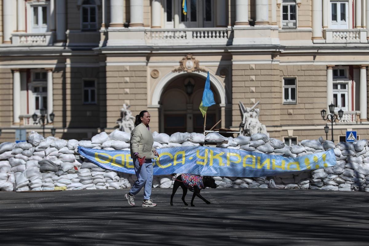 Una mujer ucraniana camina con su perro junto a una barricada con un cartel que dice ¡Odesa es Ucrania!, en la ciudad de Odesa, en el sur de Ucrania.