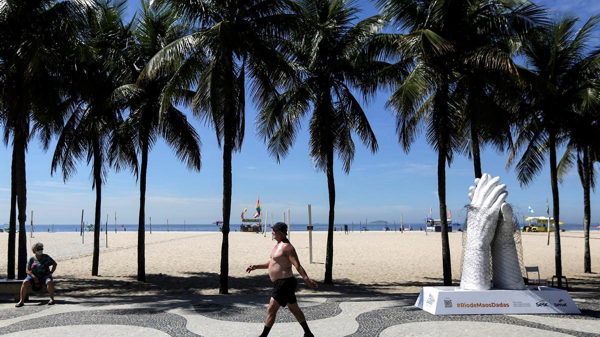 Un hombre pasea en una playa de Río de Janeiro frente a una escultura homenaje a las víctimas del covid.