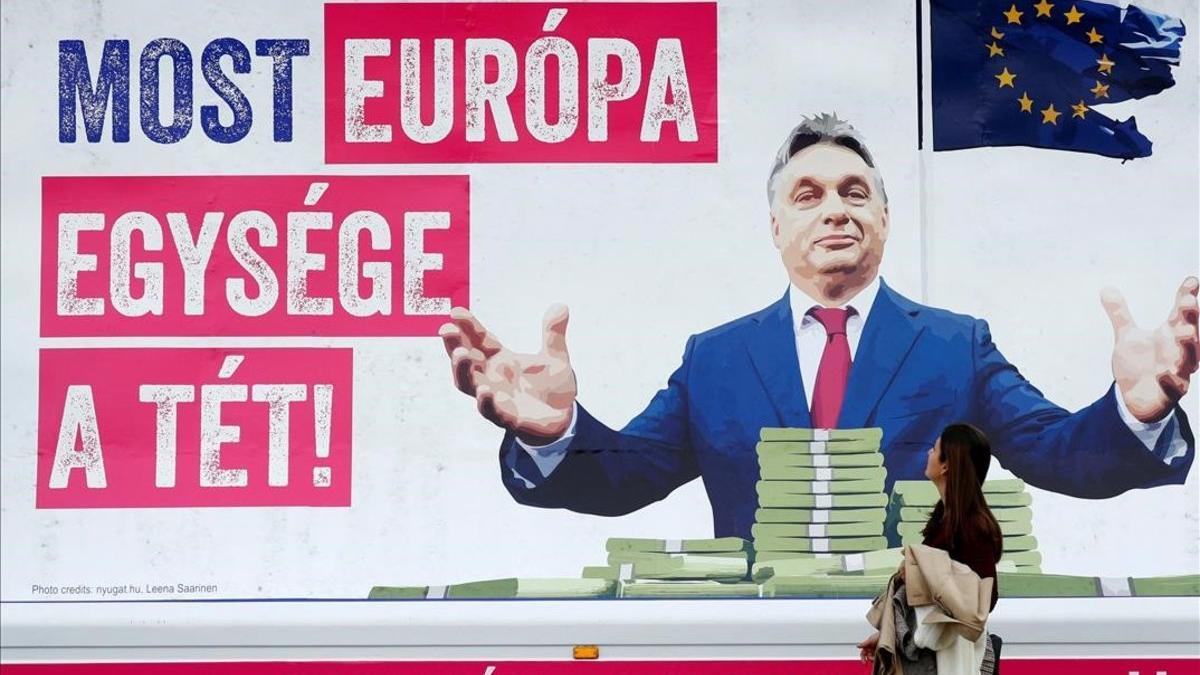 Una mujer pasa junto a un cartel en el que se critica al primer ministro de Hungría, Viktor Orban, por amenazar la unidad de Europa, en los alrededores del Parlamento Europeo, en Bruselas.