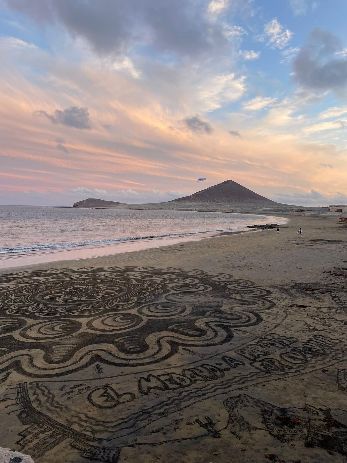 Un mandala en la arena de El Médano con Montaña Roja de fondo junto al atardecer