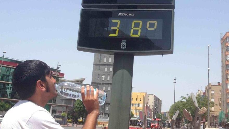 Un joven bebe agua junto a un termómetro que marca 38 grados, este sábado en Murcia.