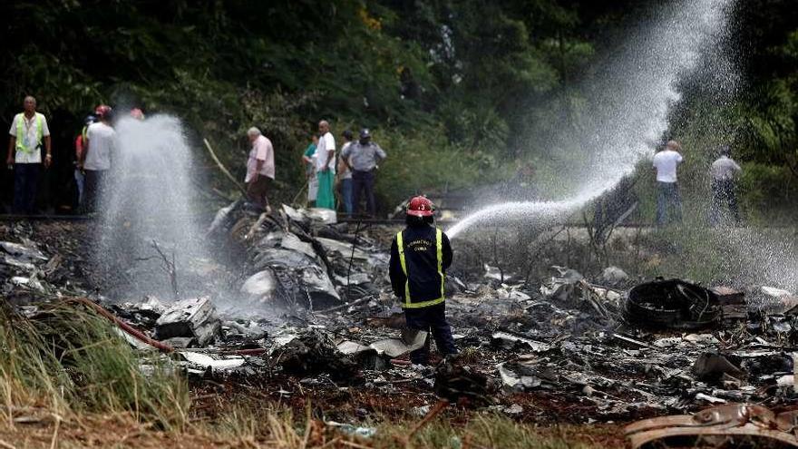 Los bomberos mojan parte de los restos del avión siniestrado. // Efe