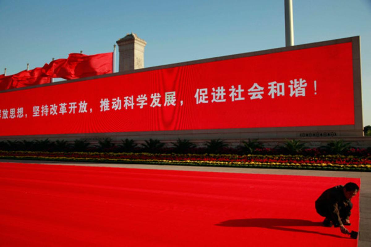 Un home col·loca una alfombra vermella a la plaça de Tiananmen, a Pequín, com a part dels preparatius de la festa nacional xinesa que se celebra demà. Darrere seu una pantalla enorme mostra l’eslògan: Allibera els teus pensaments, obre la teva ment, avança el progrés científic i desenvolupa l’harmonia social.