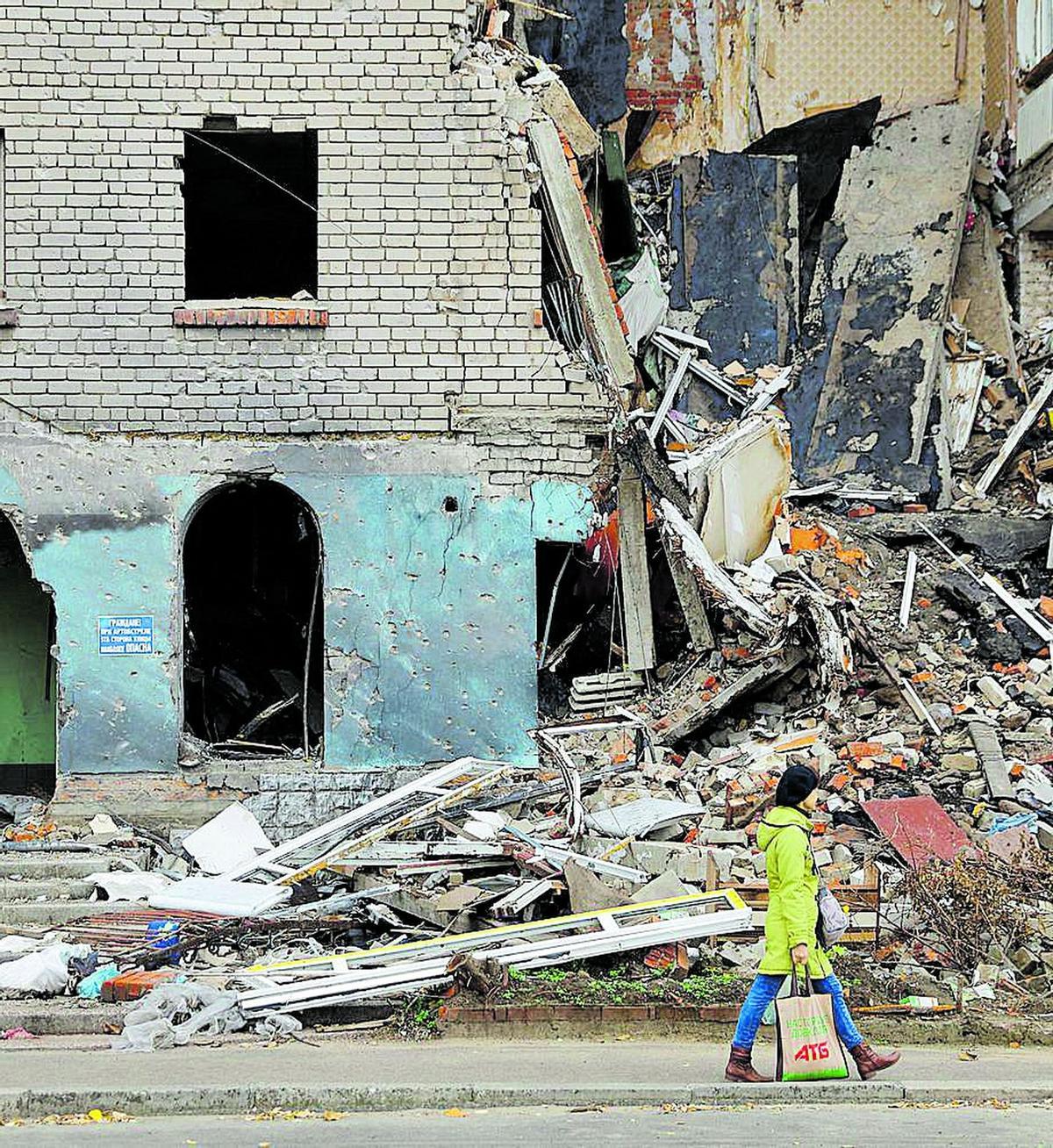 Una mujer camino por una calle de Jersón, la ciudad de la vila-realense Sonia Bespalova, con un edificio destruido por las bombas como fondo.