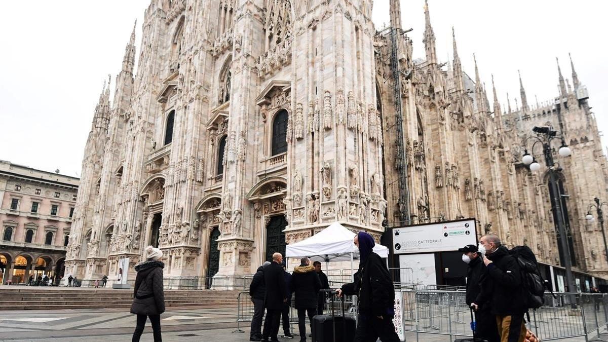 Turistas con mascarillas pasan por delante de la catedral de Milán, en Lombardía.