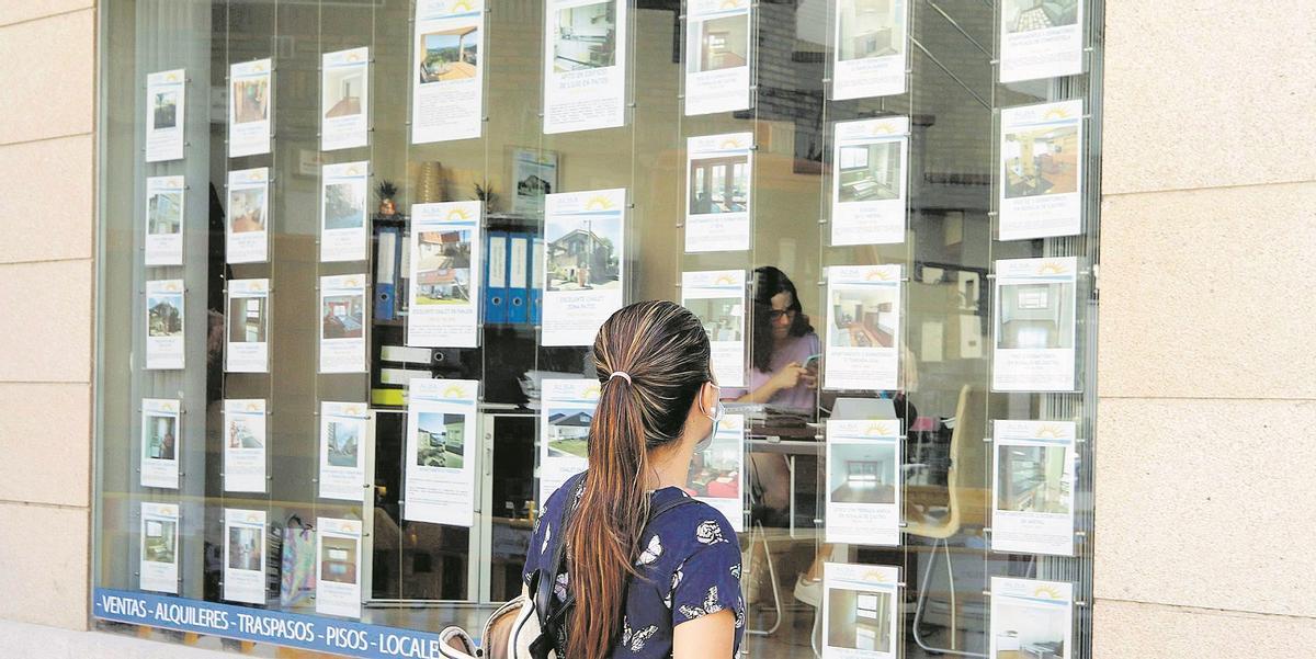 Una joven mira los anuncios de pisos en el escaparate de una agencia inmobiliaria.