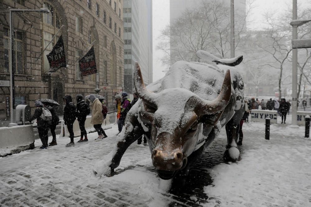 Pedestrians walk past a snow covered bull ...