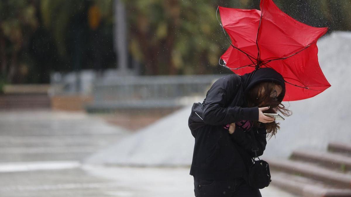Una mujer lucha contra el fuerte viento que se registra este miércoles en Málaga.