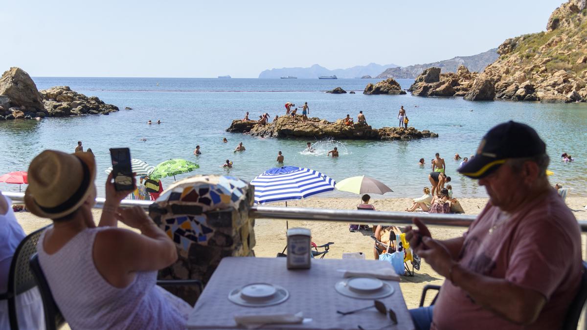 Dos turistas comen frente a cala Cortina, en Cartagena.