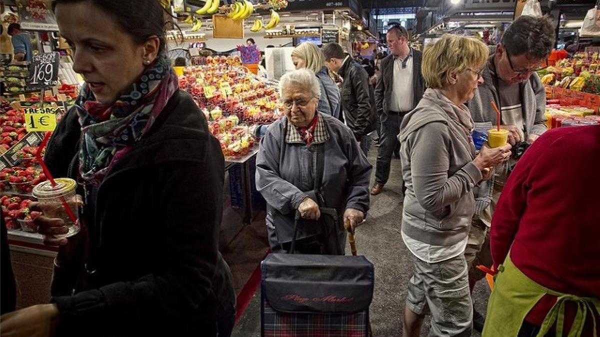 Una vecina, apoyándose en el carro y el bastón, intenta comprar en la Boqueria el pasado viernes entre turistas