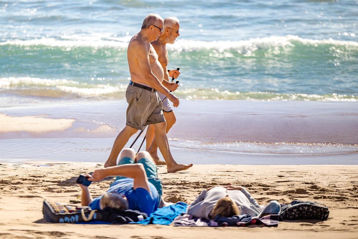 Dos personas mayores paseando por la playa de Benidorm.