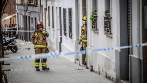 Dos bomberos ante la puerta del bloque parcialmente derrumbado el 6 de febrero en la calle Canigó de Badalona