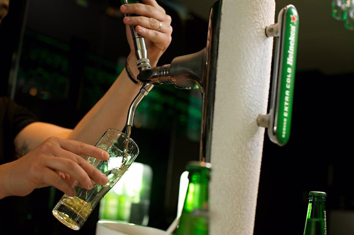 Un camarero rellena un vaso con la cerveza Heineken.