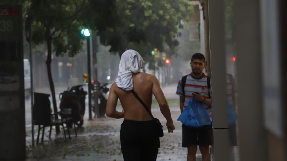 Un hombre camina por Zaragoza con una camiseta en la cabeza para cubrirse de la lluvia