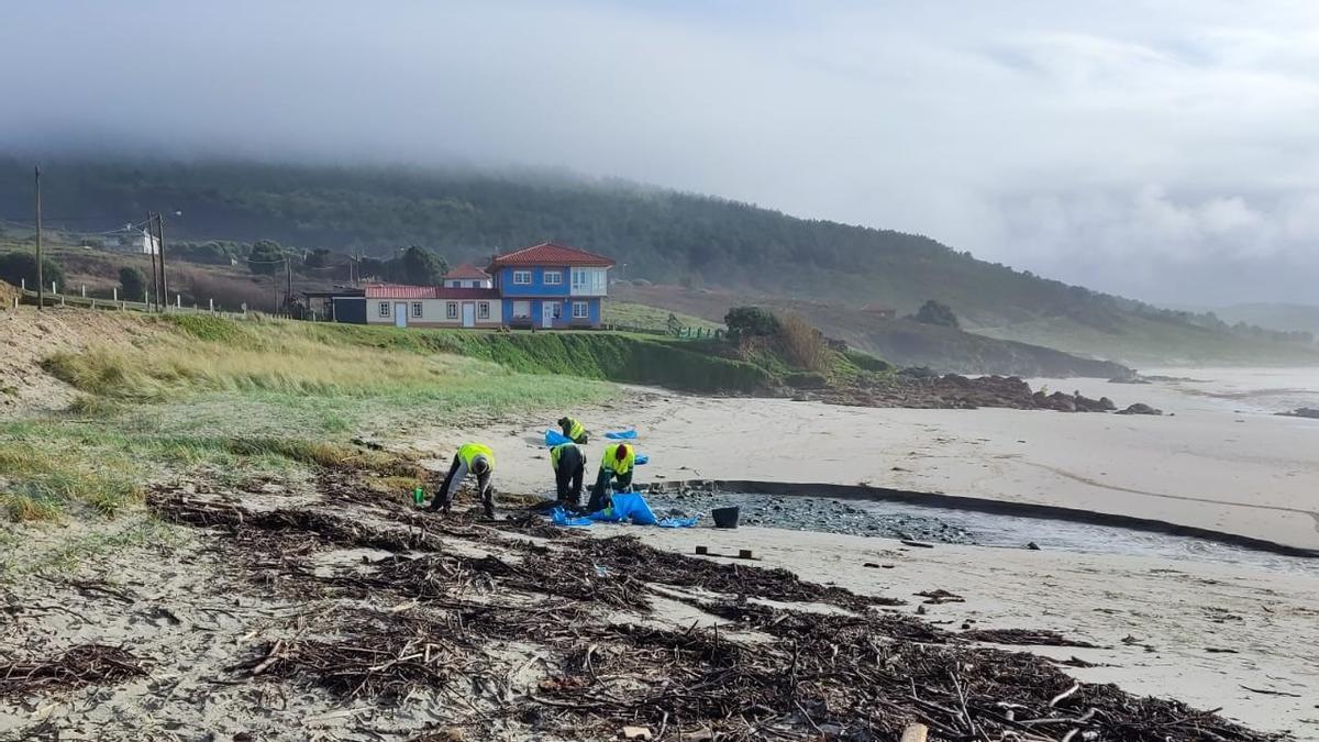 Operarios contratados por la Xunta retirando pélets este lunes en la playa de Nemiña, en Muxía