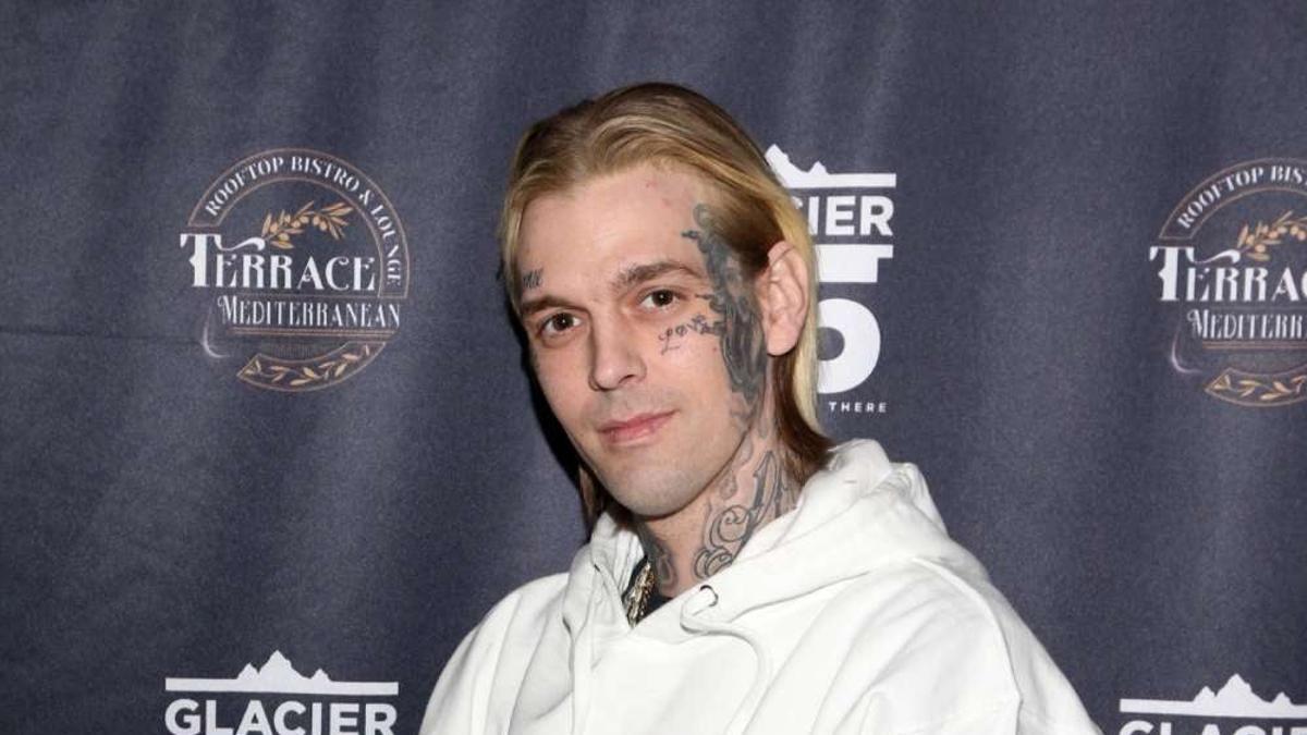 Aaron Carter con pelo medio largo, tatuajes y sudadera blanca