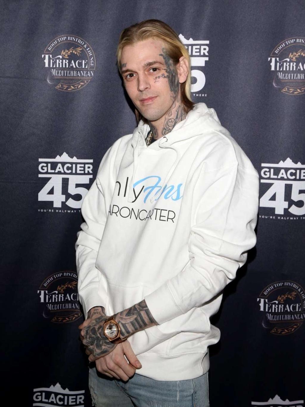 Aaron Carter con pelo medio largo, tatuajes y sudadera blanca