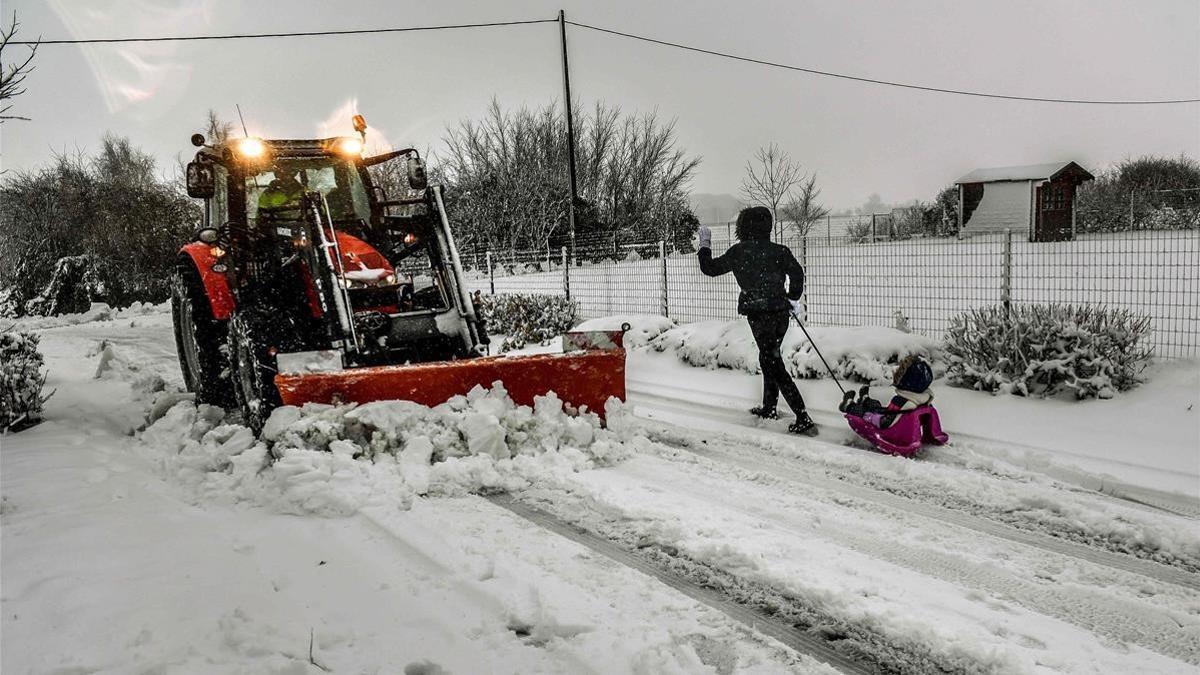 Un niño tirado por un trineo pasa delante una máquina quitanieves en Godewaersvelde el norte de Francia.