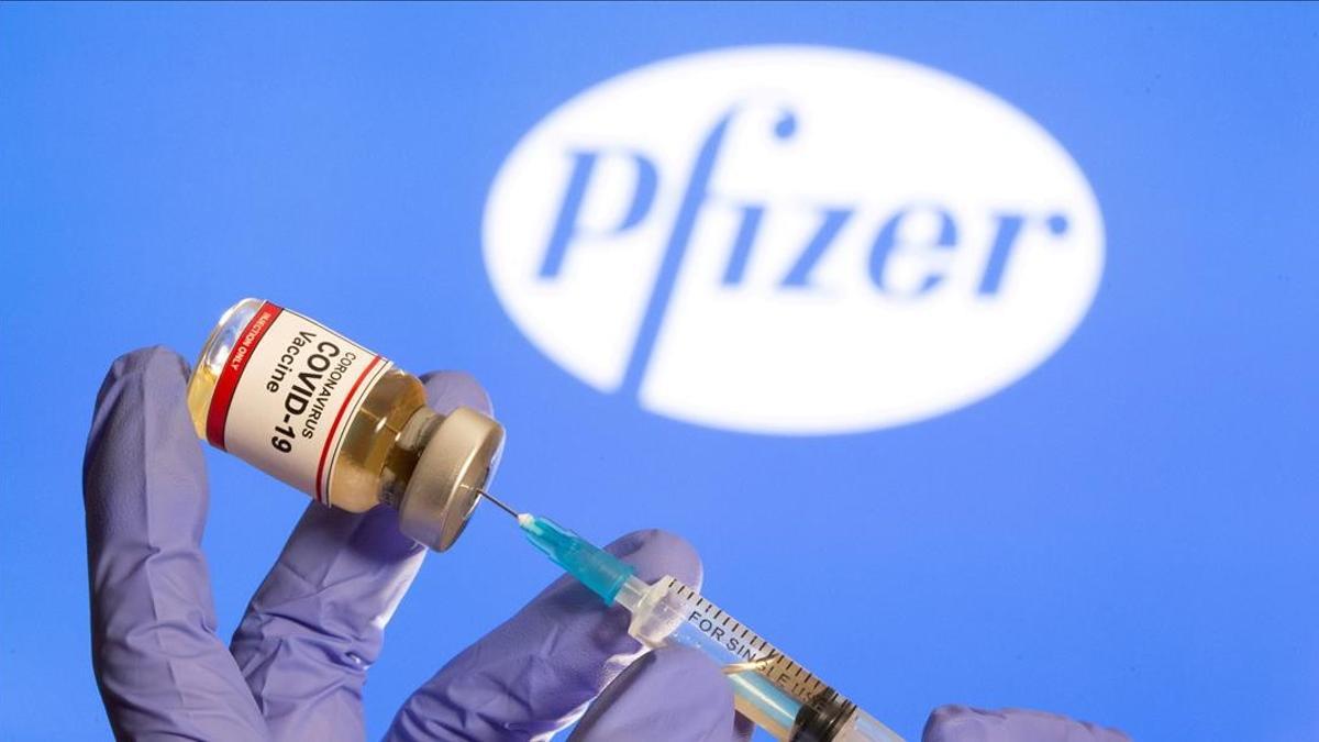 Una mujer sostiene una pequeña botella etiquetada con una etiqueta adhesiva de vacuna contra el coronavirus y una jeringa médica frente al logotipo de Pfizer