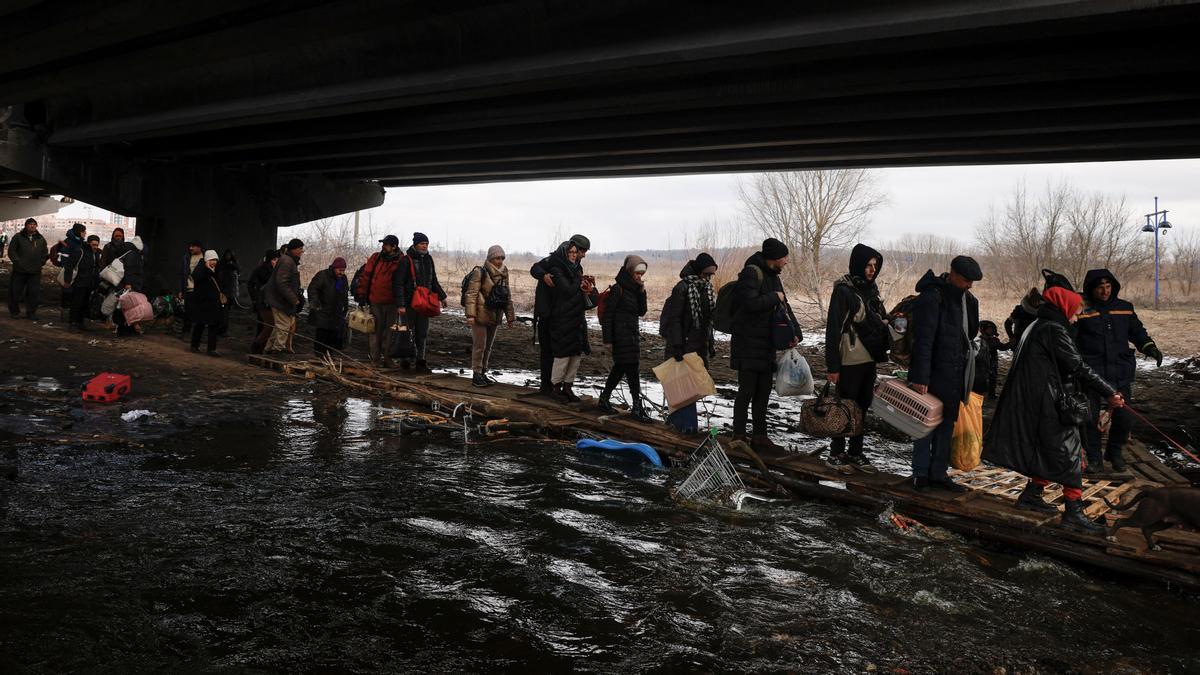 Las personas que huyen del avance de las fuerzas rusas cruzan a través de tablones de madera el río Irpin, debajo de un puente destruido mientras continúa el ataque de Rusia contra Ucrania.