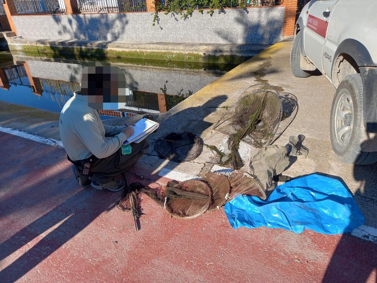 Un agente medioambiental registrando el hallazgo y la retirada de la red ilegal en un canal de la marjal de Nules.