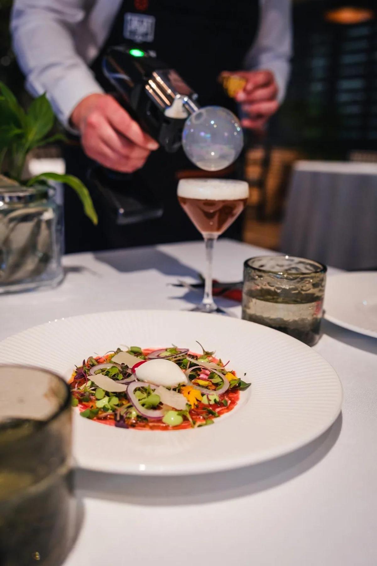Un cóctel junto al plato presentado en mesa durante el pase en  Versátil