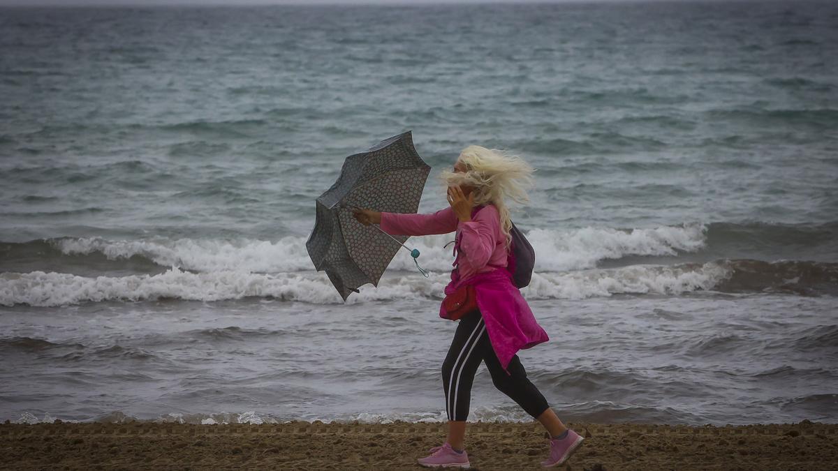 Una mujer camina como puede ayer por la playa del Postiguet con lluvia y viento