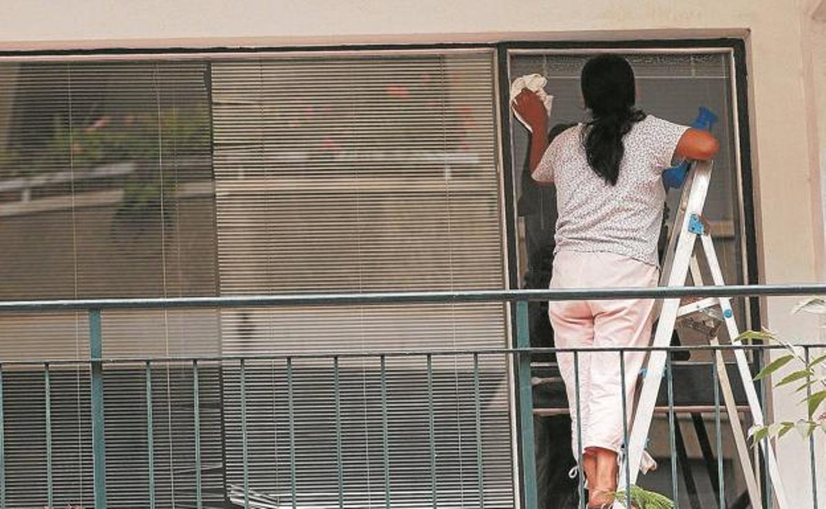 Una empleada de hogar limpia las ventanas de una terraza.