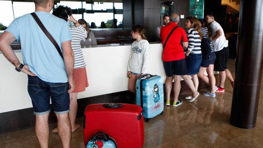 Varios turistas esperan para registrarse en la recepción de un hotel de Gijón.