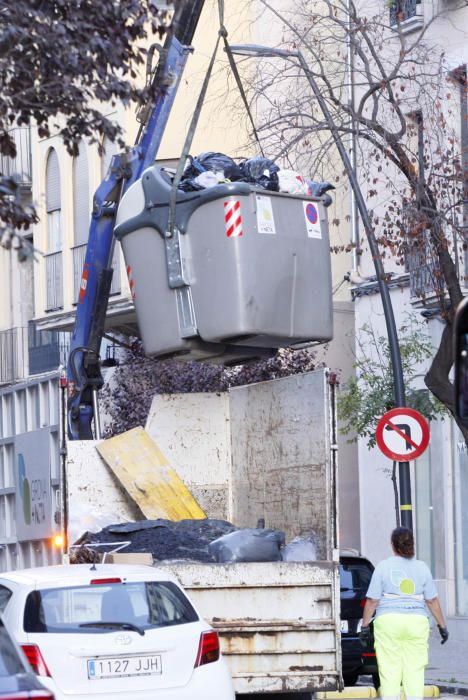 Carrers amb restes de mobiliari urbà cremat, contenidors per terra i treballadors de la brigada treballant