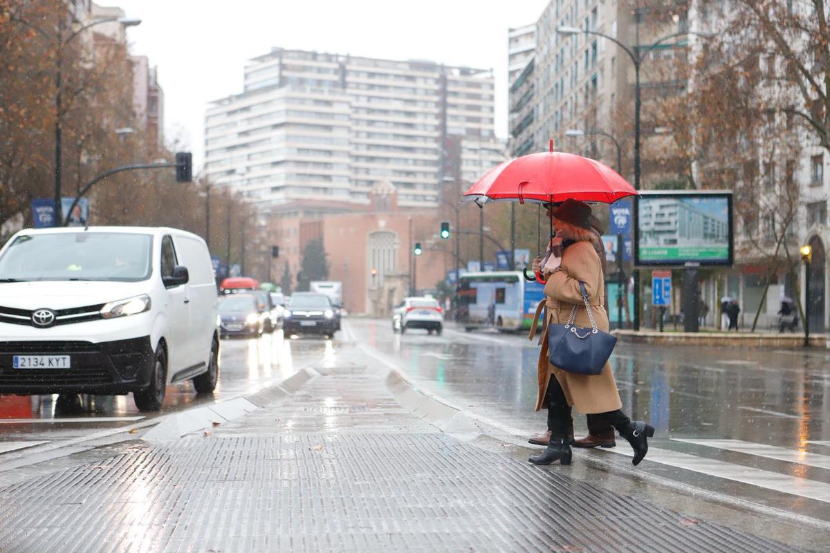 Una pareja cruza una calle del centro de Zaragoza este jueves protegiéndose de la lluvia