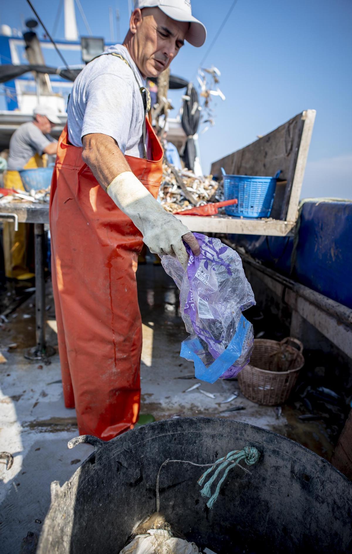 Un pescador sacando del mar una bolsa de plástico.