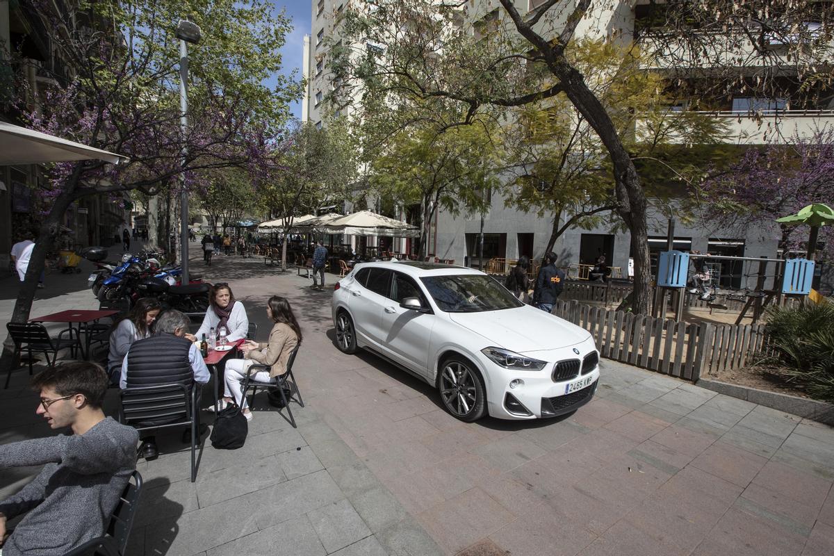 Un coche circula entre una terraza y un parque infantil, en Enric Granados.