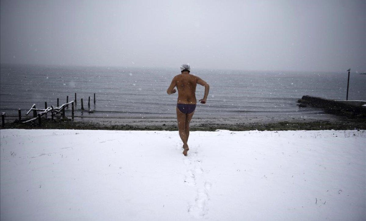 Un nadador corre hacia el mar en una playa cubierta de nieve en la ciudad griega de Tesalónica.