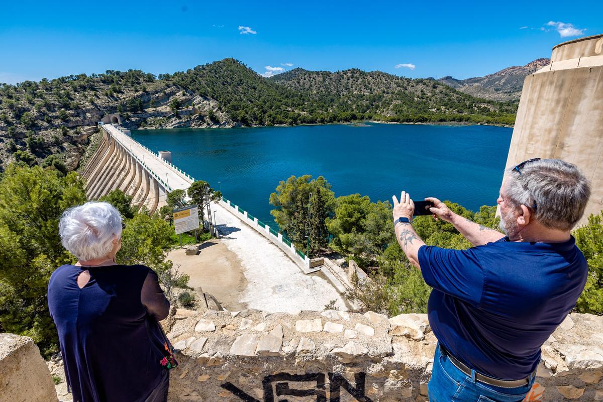 Dos personas observan el pantano del Amadorio lleno en estos días.