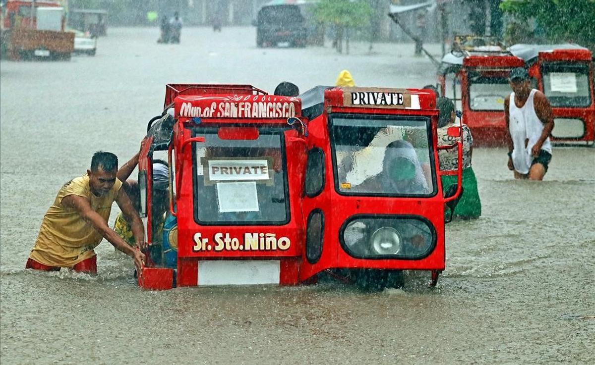 Un grupo de gente empuja un triciclo medio sumergido en una calle inundada por las fuertes lluvias originadas por la depresión tropical Vicky, en la ciudad de San Francisco, en la isla de Mindanao, Filipinas, en diciembre del 2020.