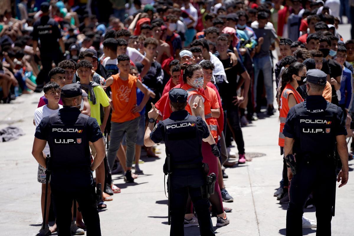 Policías ante menores marroquís alineados en las naves de El Tarajal, Ceuta. Mayo de 2021