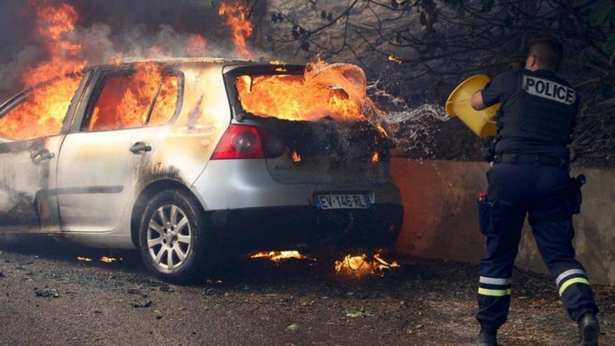 Un agent de policia intenta apagar el foc en un cotxe durant un incendi forestal a Marsella, aquest dimarts.