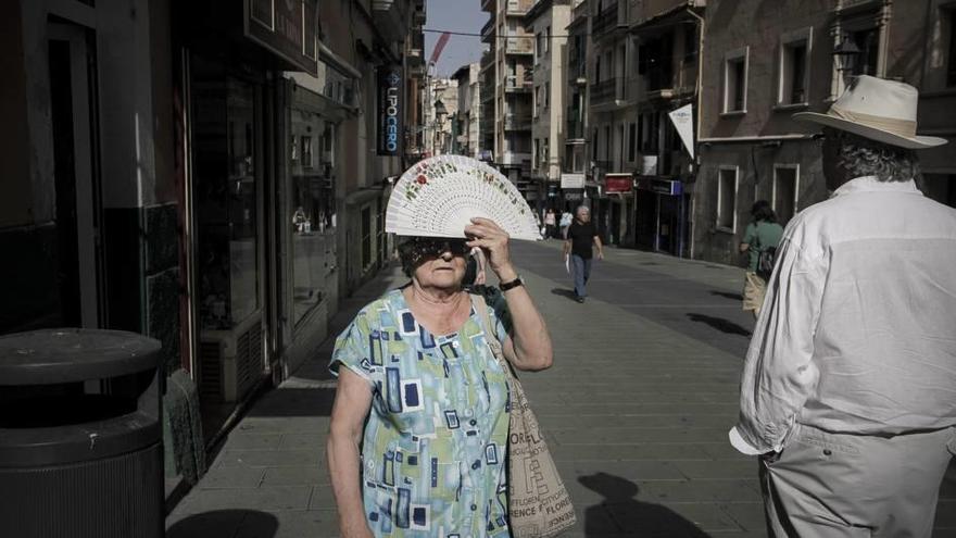 Una mujer se tapa el sol con el abanico en plena ola de calor en Palma.