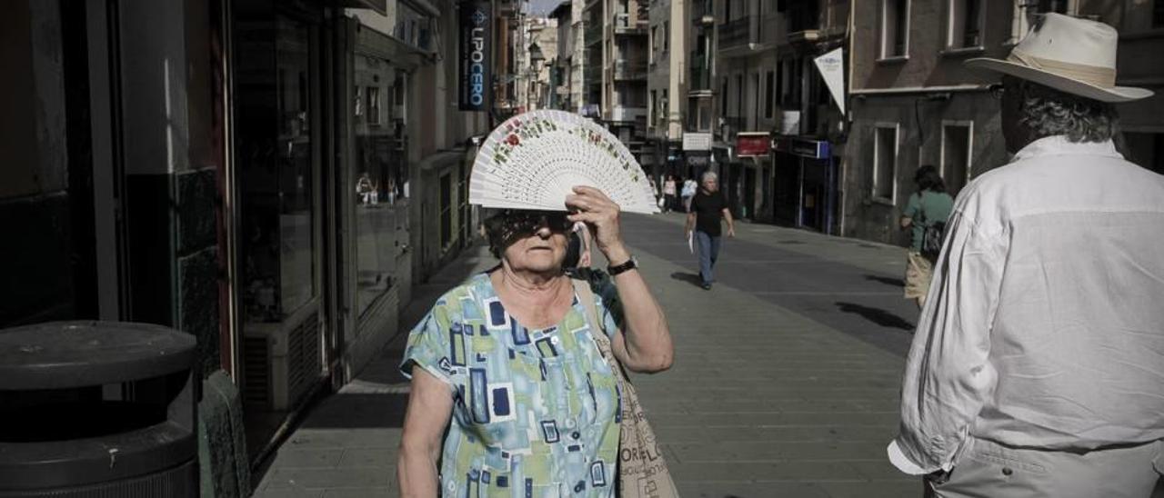 Una mujer se tapa el sol con el abanico en plena ola de calor en Palma.