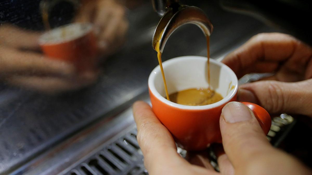 Una persona aguanta una taza para recoger café en una cafetera automática.