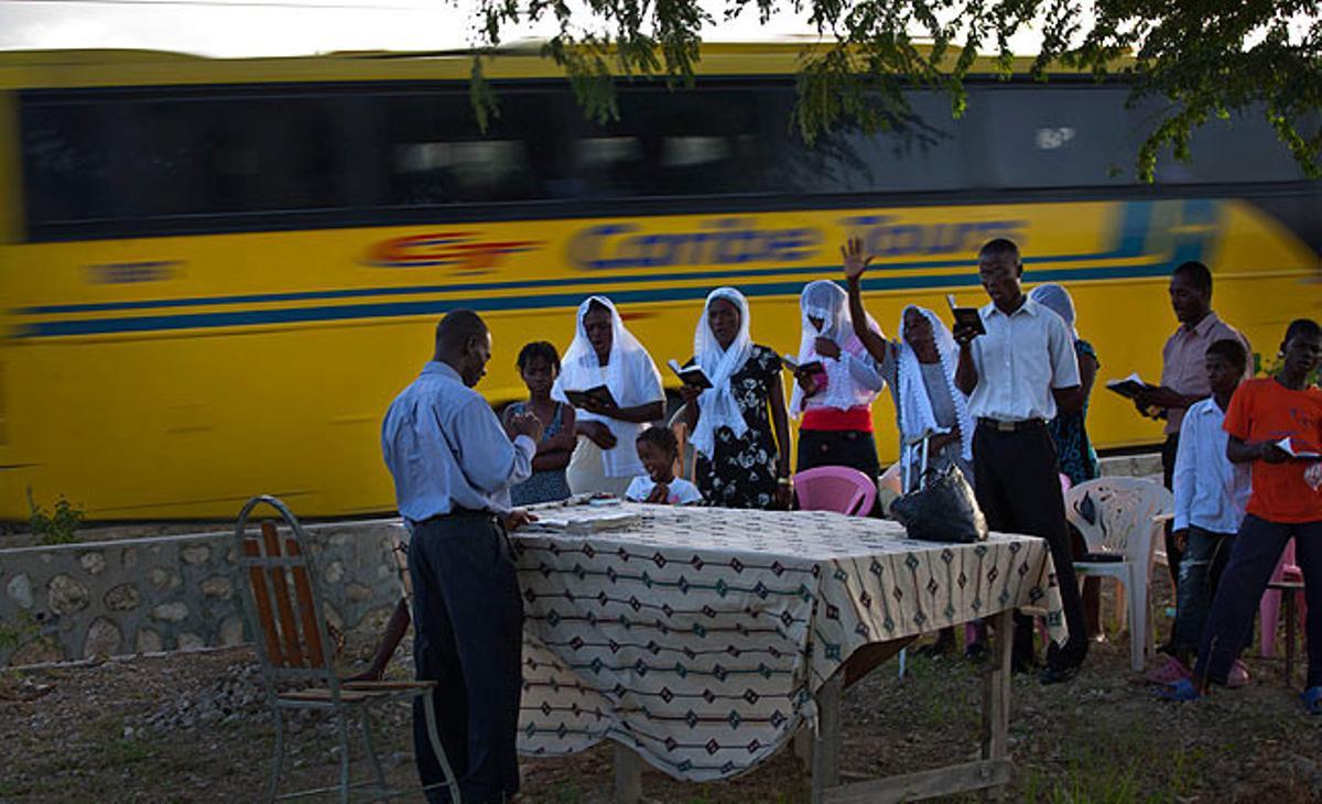 Un autobús passa davant una improvisada capella on un grup d’haitians està resant, a Malpasse (Haití).