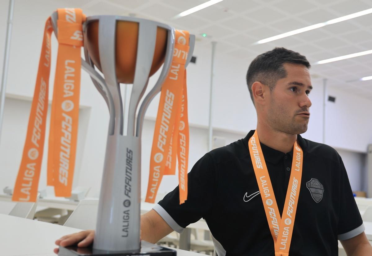 El técnico Óscar Morales toca el trofeo de la FUTURES durante la entrevista, en la sala de prensa del Martínez Valero.