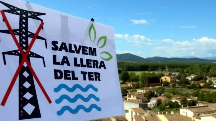 En primer terme, un cartell de Salvem la Llera del Ter; al fons, paisatge que queda afectat per la línia.