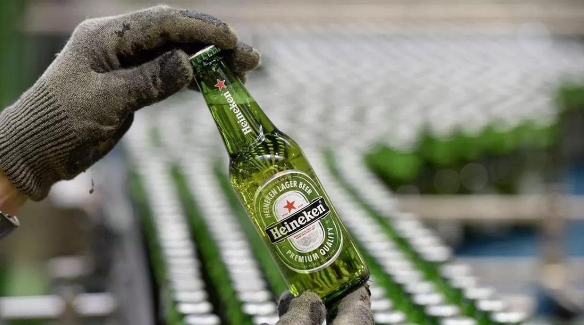 Un operario muestra una botella de cerveza en una cadena de producción de una fábrica.