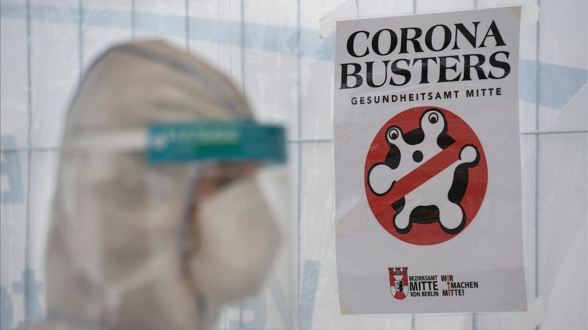 Un sanitario con equipo de protección y máscara junto a un cartel de Corona Busters colgado en un hospital de Berlín